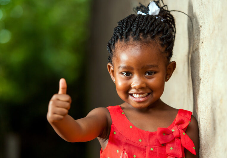 Portrait of happy little african girl doing thumbs up sign outdoors.